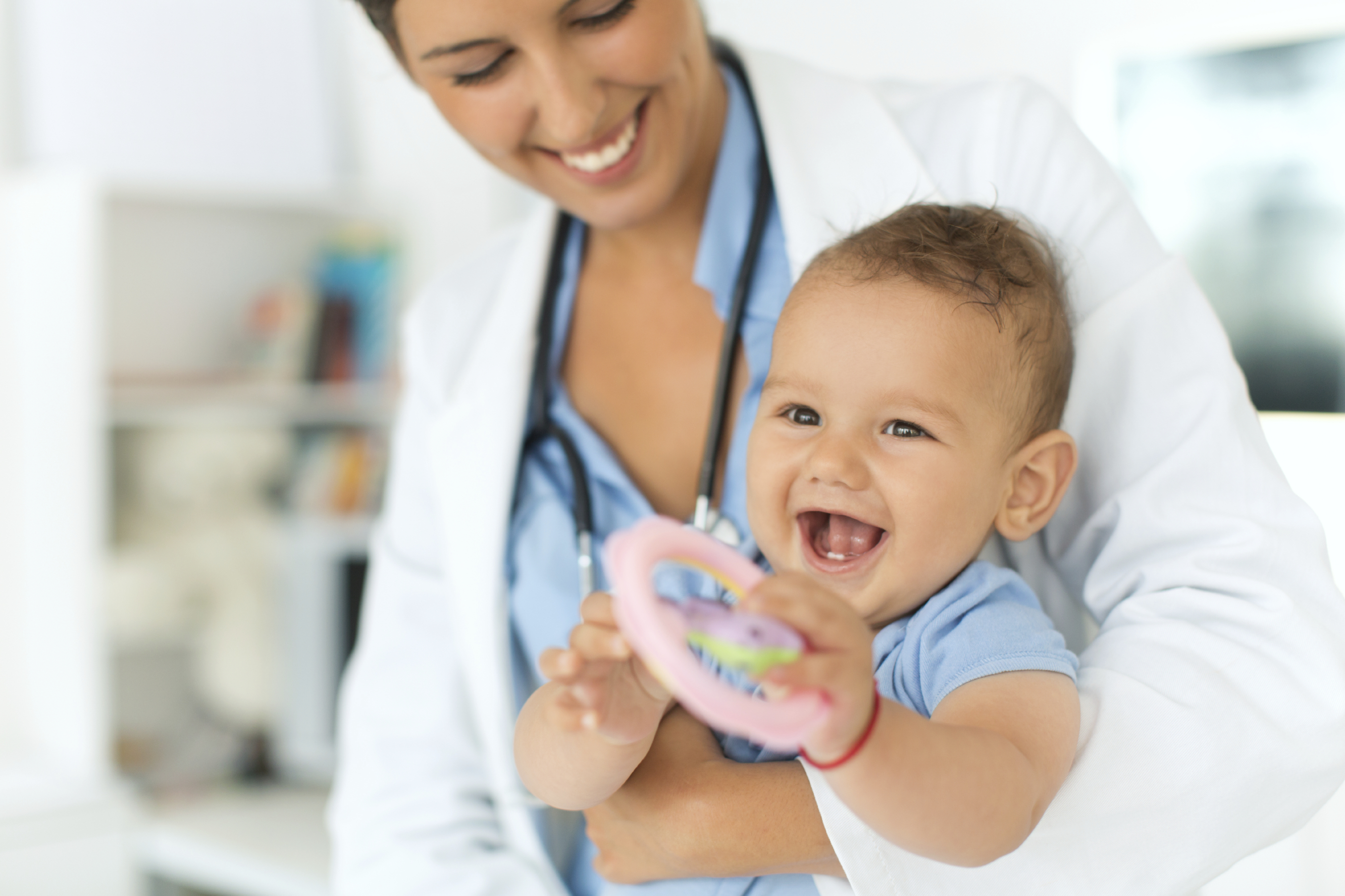 Medic pediatru zâmbind care ține un bebeluș care râde, într-un cabinet medical luminos